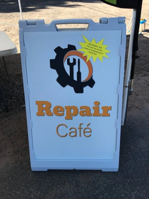 A white sandwhich board placed on a sidewalk that says 