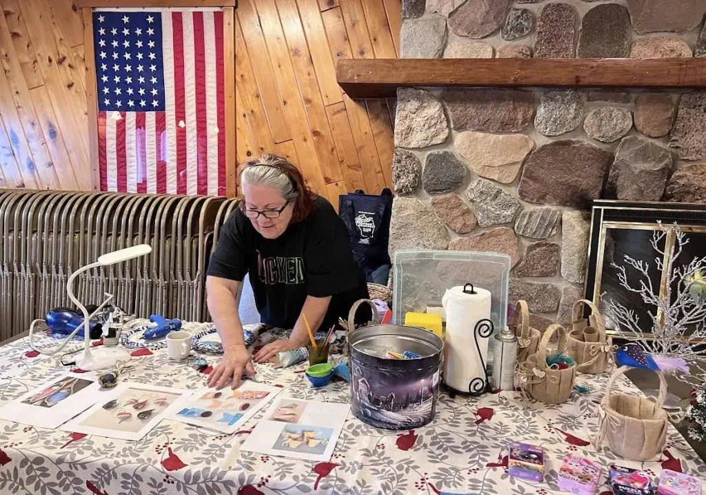 A woman standing behind a table setting up and displaying a variety of craft supplies.