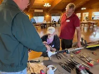 Three men around a table with tools on it.