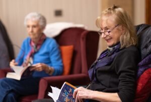 Senior women comfortably reading in a cozy indoor setting, smiling and enjoying a book club session.